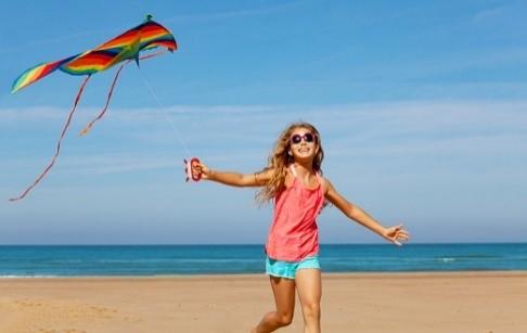 Picture with alternative text: Girl runs on the beach and flies colorful kite. 